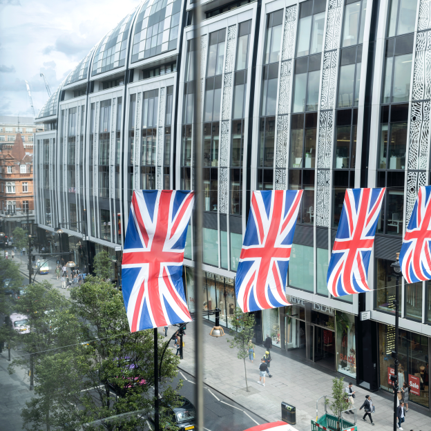 A line of Union Jack flags hanging between two glass-panelled office buildings over a busy main road of London
